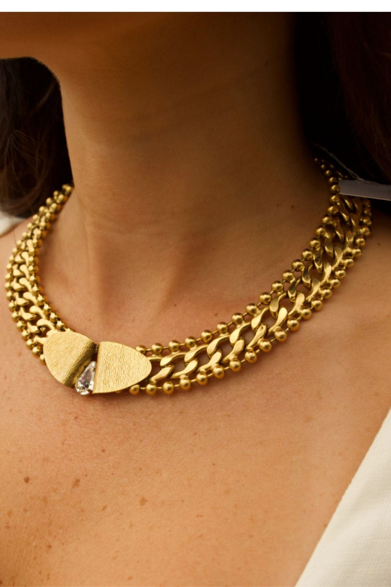 Close-up of handcrafted brass necklace with 22K gold plating and crystal teardrop accent