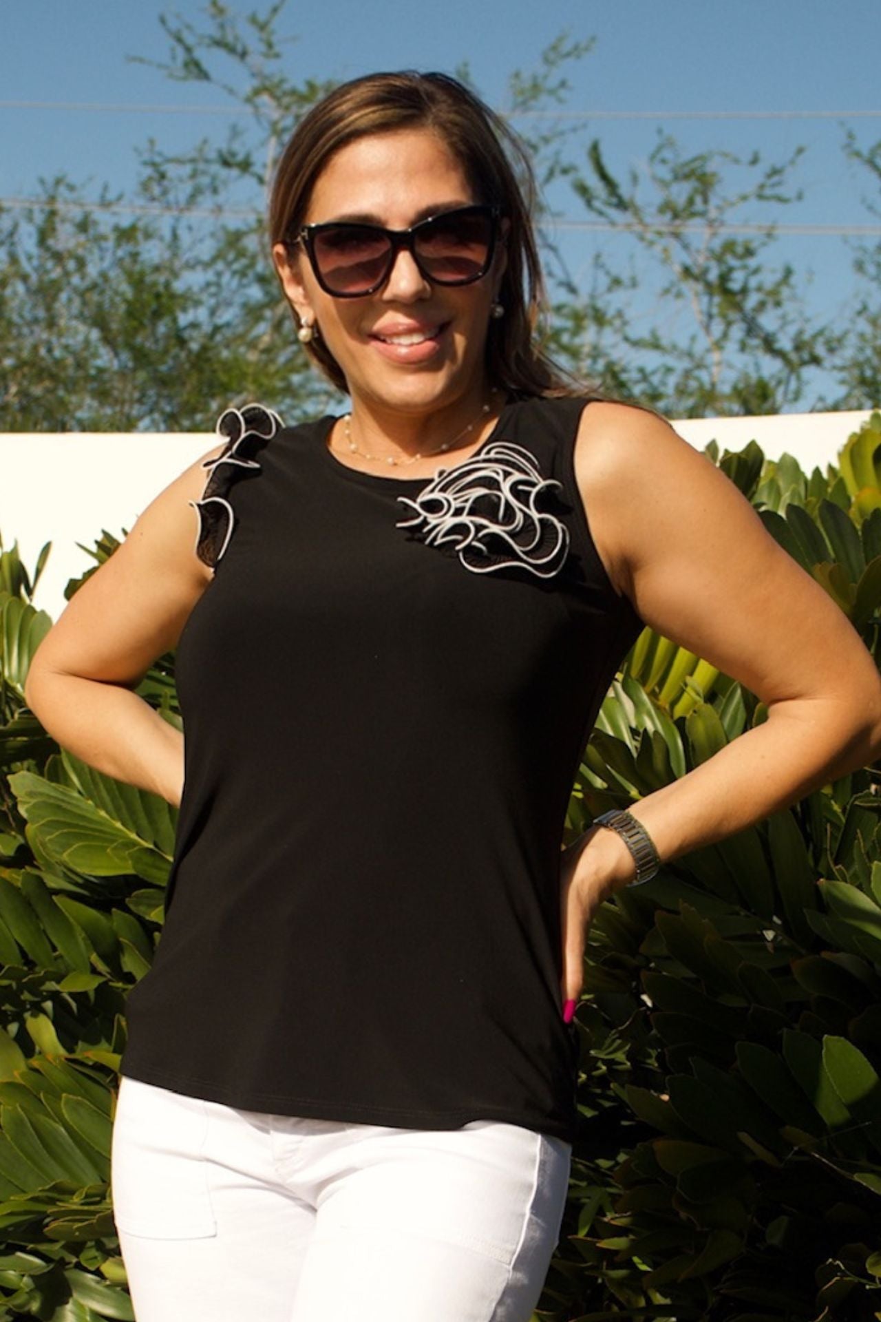 Woman wearing black sleeveless jersey top with white ruffle trim and floral embellishment, standing elegantly