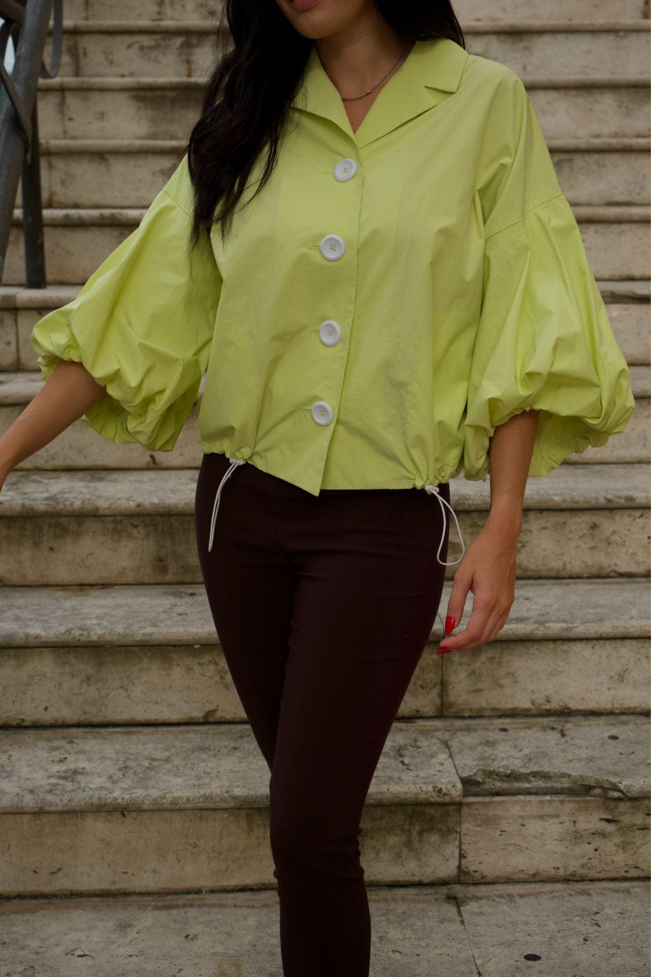 Woman wearing lime green crop jacket with puff sleeves and white buttons, standing on stairs.