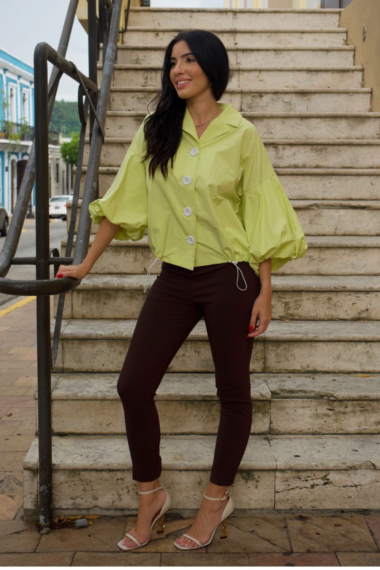 Woman wearing lime green crop jacket with puff sleeves and white buttons, standing on stairs.