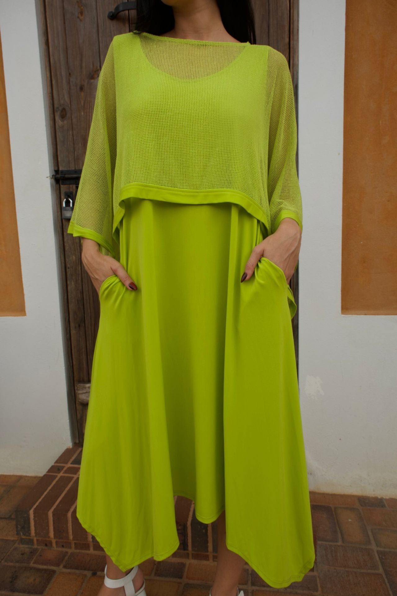 Woman wearing a lime green sleeveless jersey dress with a mesh overlay, standing in front of a rustic wooden door.