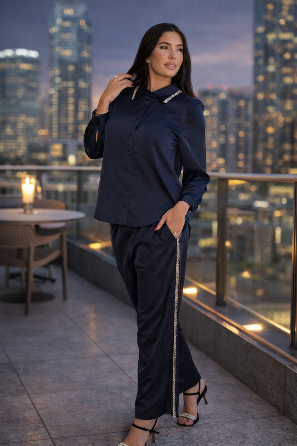 Woman wearing a navy satin blouse and matching pants set on a rooftop terrace, polished and sophisticated evening look
