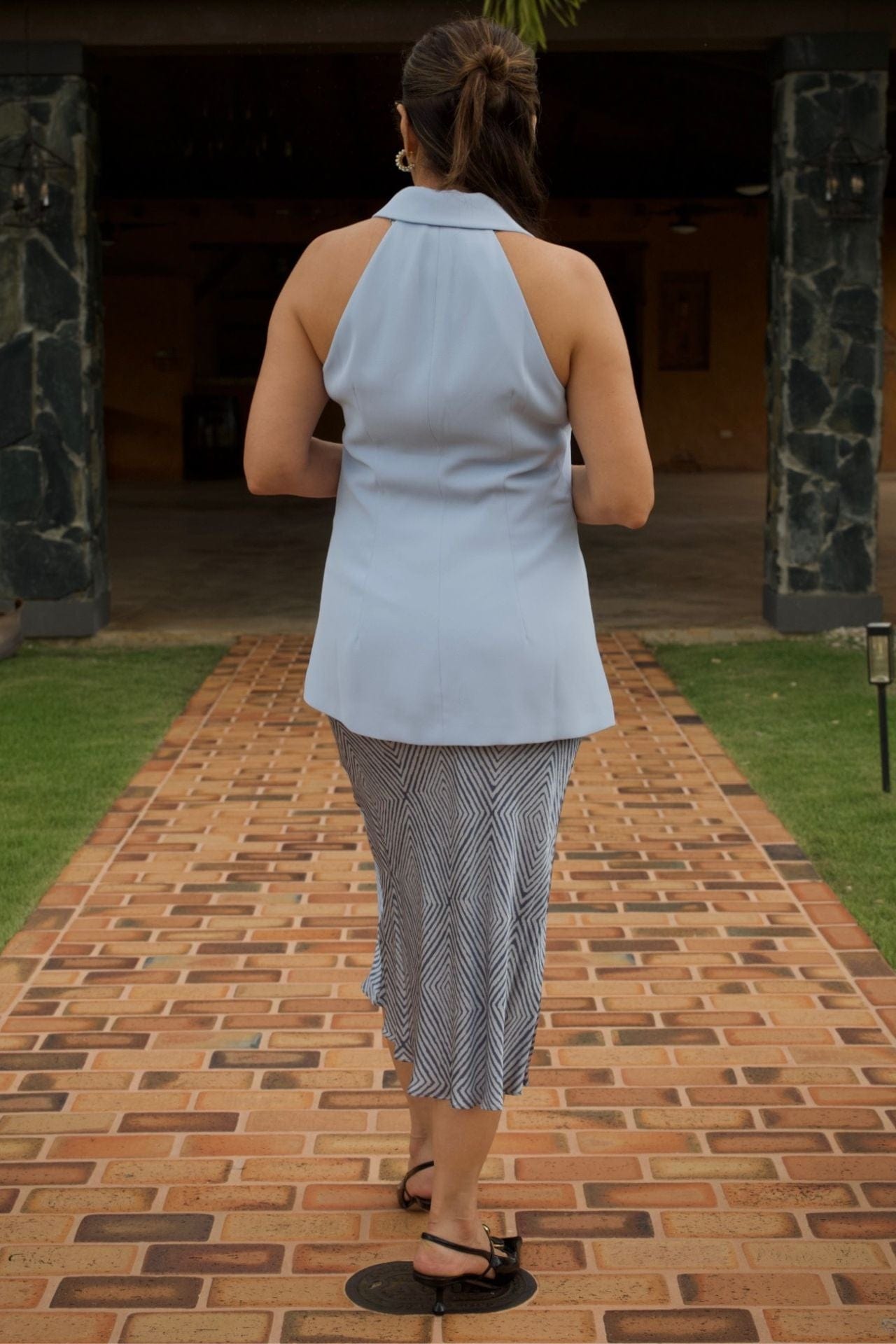 Back view of woman wearing blue sleeveless blazer with fitted collar