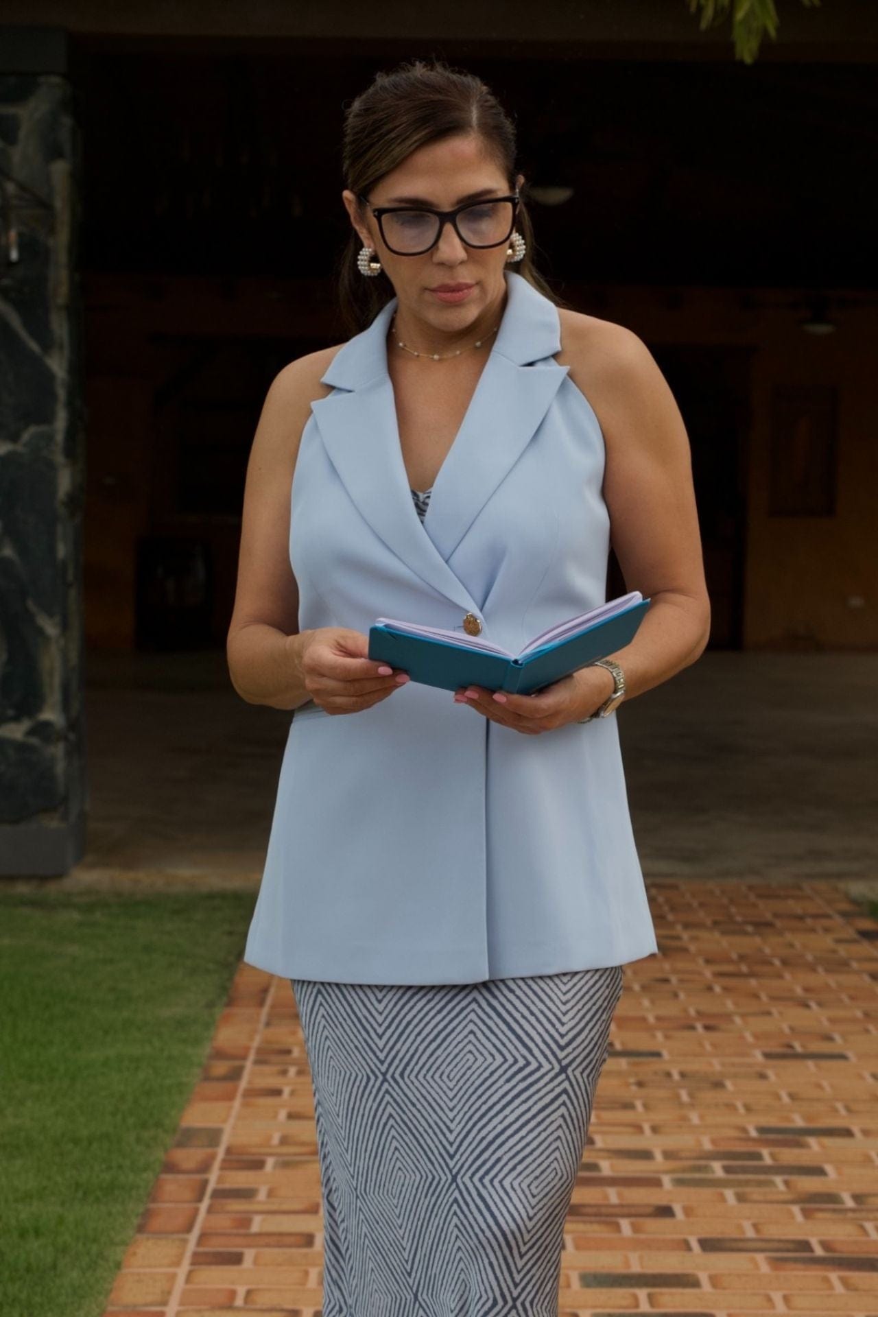 Woman in light blue blazer reading a notebook outdoors