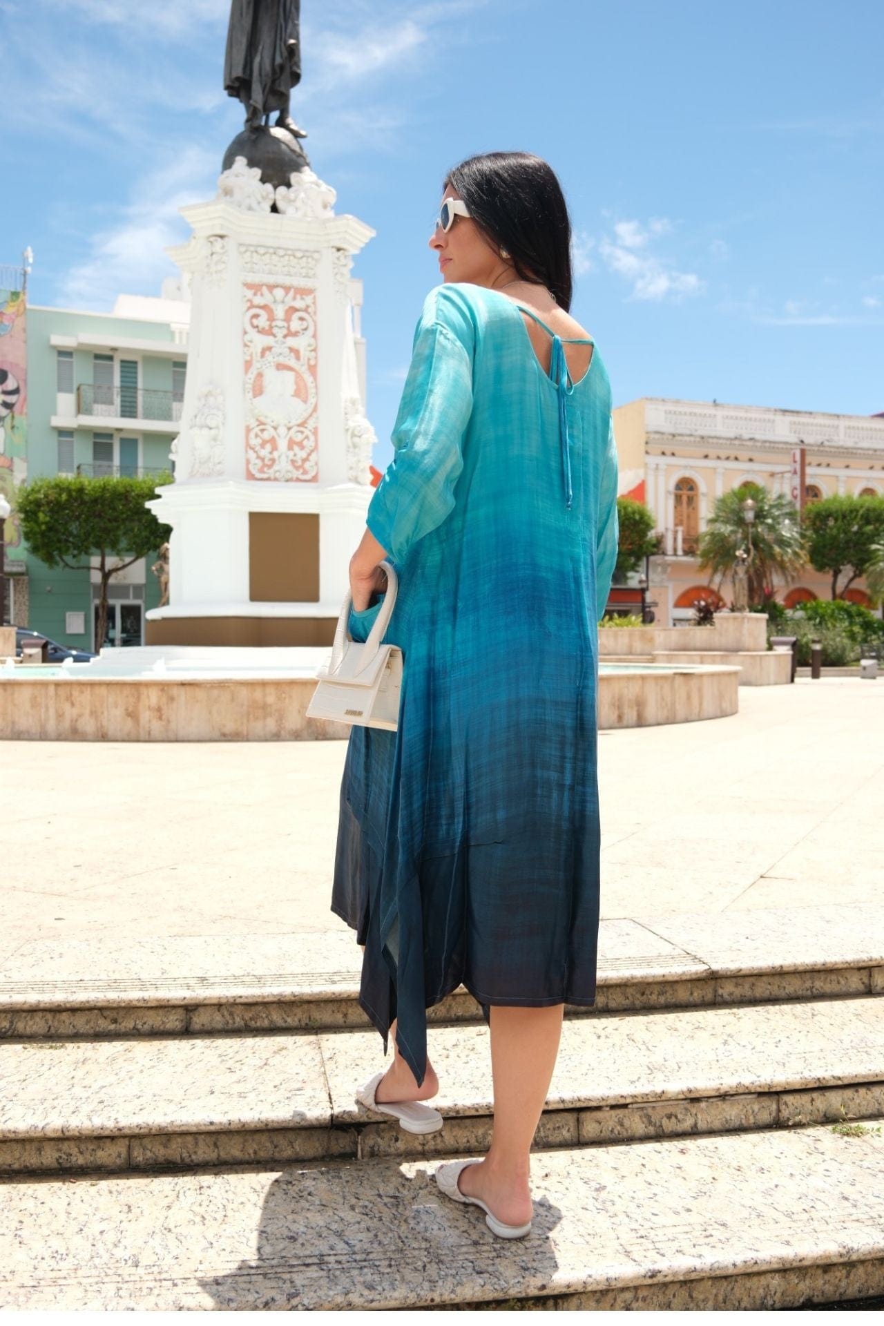 Model wearing teal ombre satin midi dress with pockets and asymmetrical hemline back view.