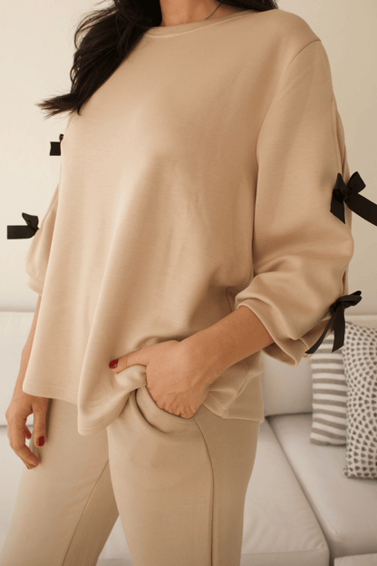 Detail of ribbon accents on the sleeve of a women's long-sleeve top, enhancing the stylish and refined look and side pockets.