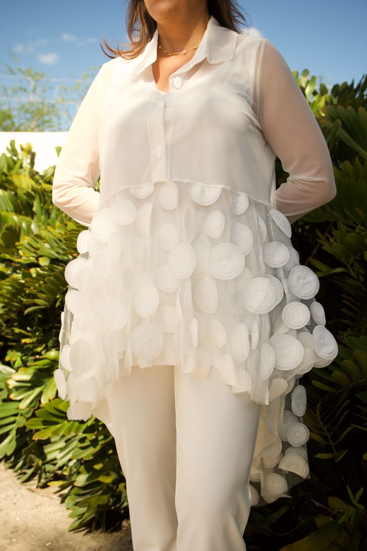 Close-up of white mesh fabric with circle detailing and soft ruffles on blouse.