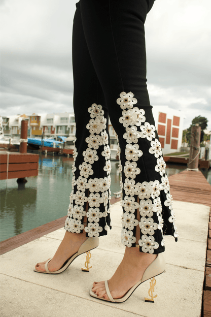 Close-up of white floral embroidery on black denim jeans, showcasing intricate stitching and fine craftsmanship.