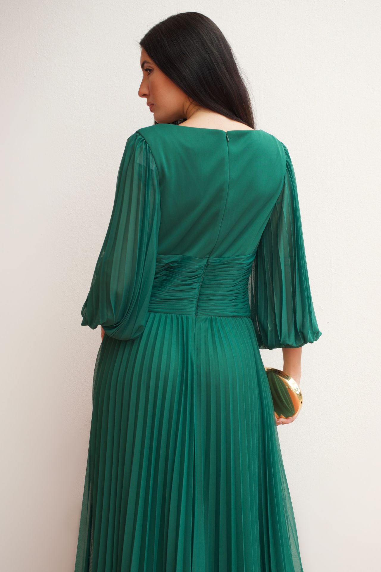 Model wearing an emerald green pleated wrap formal gown with long sleeves and flowing skirt.