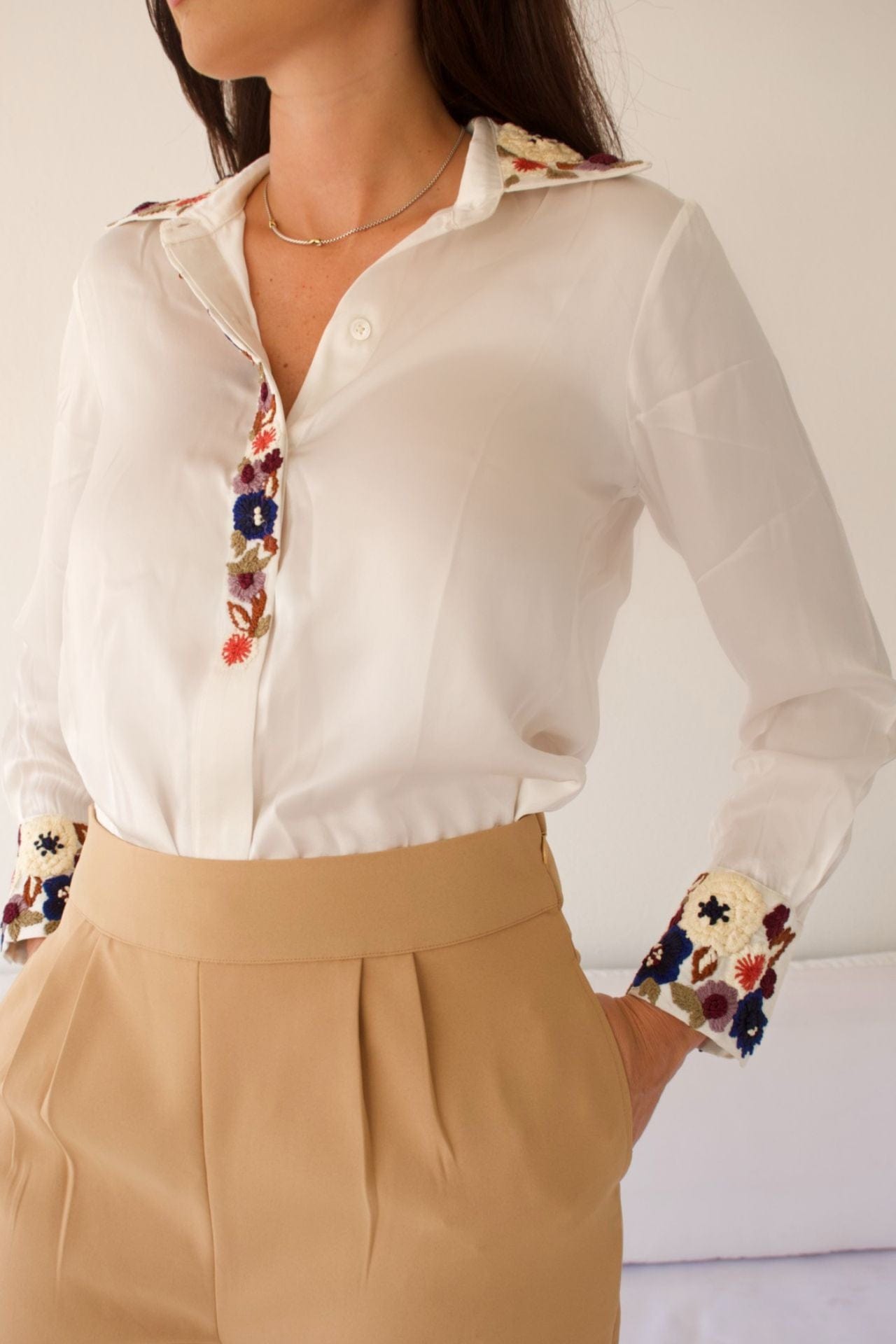 Close-up of floral embroidery on beige pants and cuff detail on blouse.

