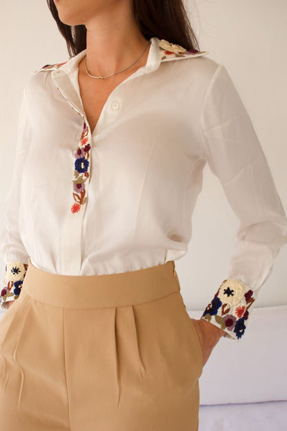 Close-up of floral embroidery on beige pants and cuff detail on blouse.

