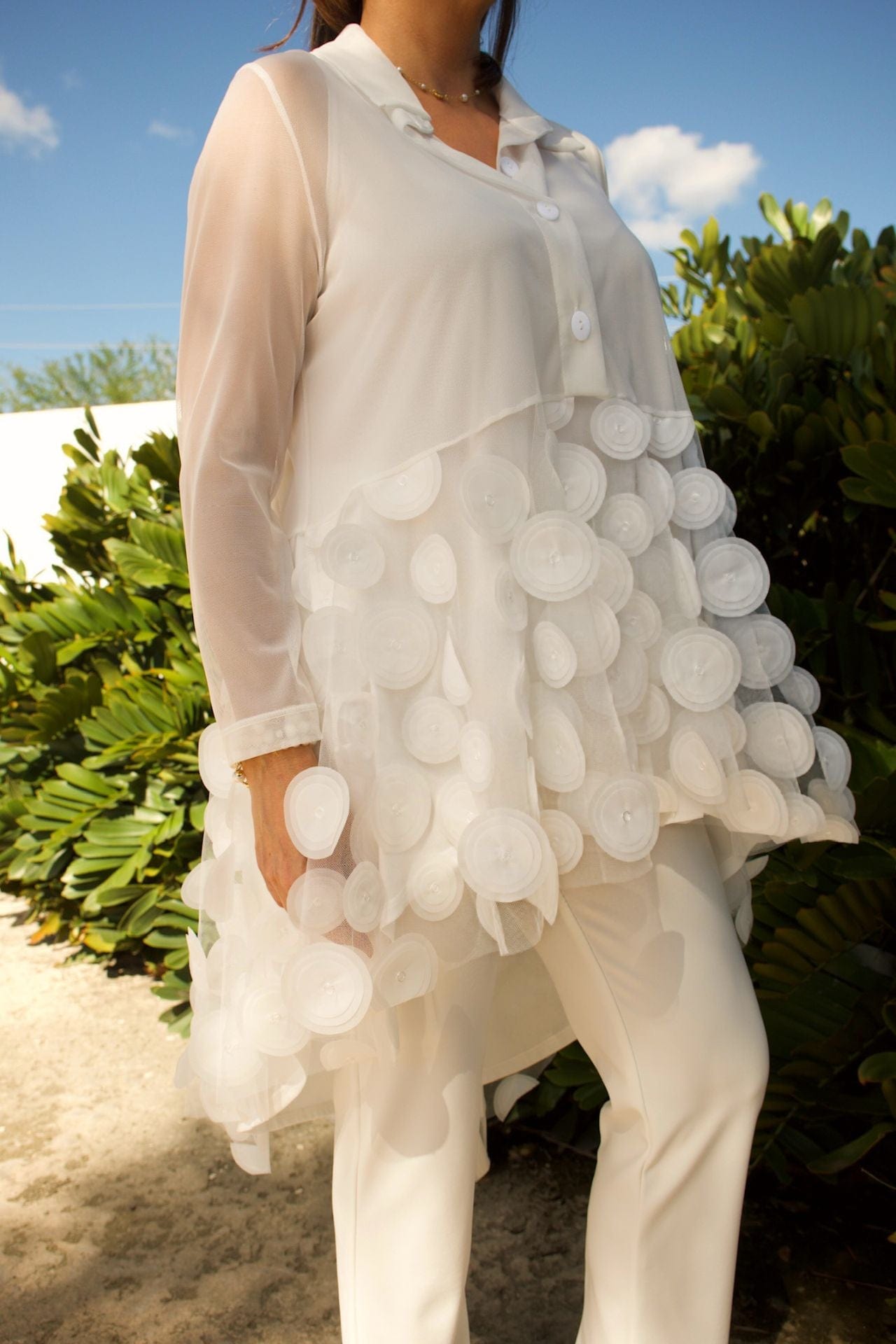Close-up of white mesh fabric with circle detailing and soft ruffles on blouse.