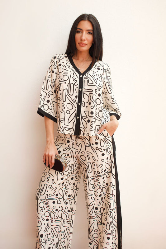 Woman wearing a black and ivory abstract print pant set with contrast trim, button-front top, and wide-leg pants, styled for an elegant daytime look.