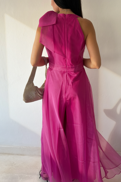 Woman wearing the Aurora Statement Jumpsuit in fuchsia with shoulder bow, wide-leg silhouette and sheer flowing overlay.