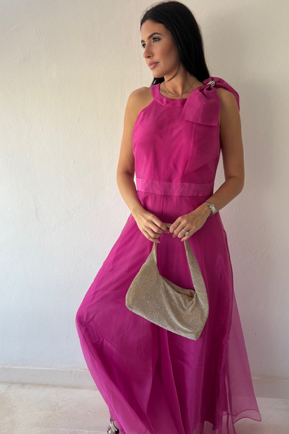 Woman wearing the Aurora Statement Jumpsuit in fuchsia with shoulder bow, wide-leg silhouette and sheer flowing overlay.