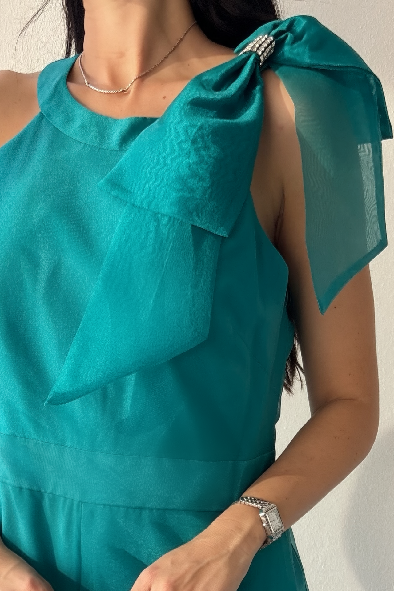 Woman wearing the Aurora Statement Jumpsuit in teal with shoulder bow, wide-leg silhouette and sheer flowing overlay.