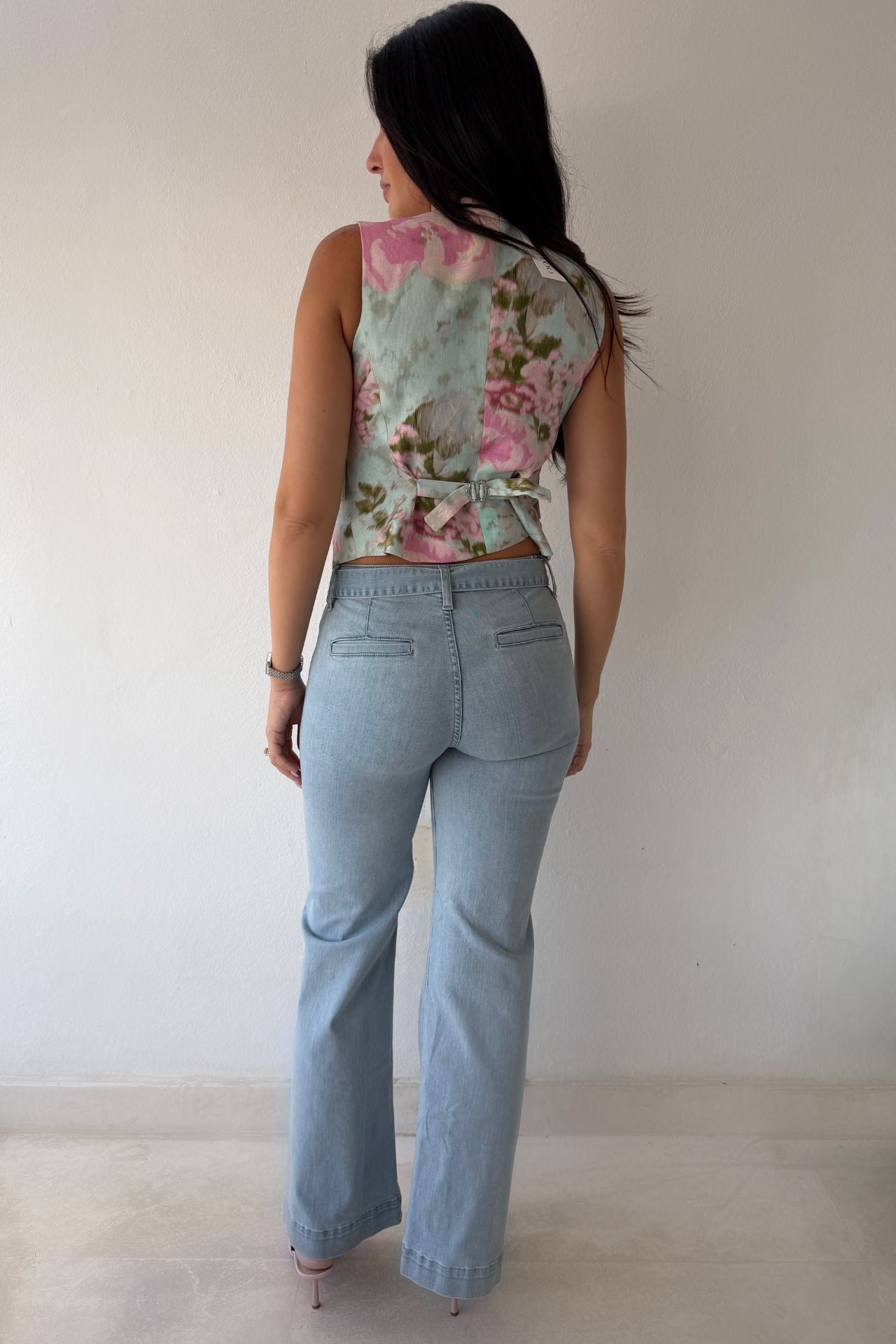 Model wearing the Blush Bloom Vest featuring a pink floral print, V-neckline, and front button closure styled with light-wash denim.
