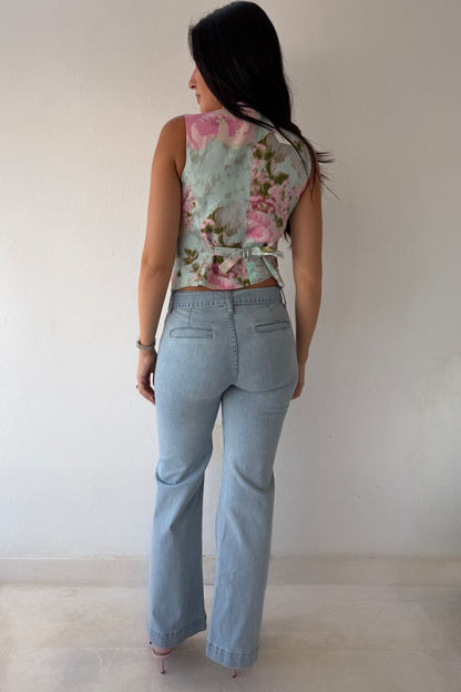 Model wearing the Blush Bloom Vest featuring a pink floral print, V-neckline, and front button closure styled with light-wash denim.