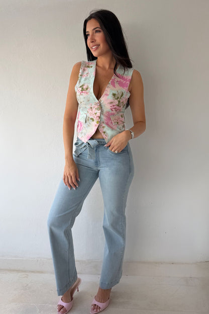 Model wearing the Blush Bloom Vest featuring a pink floral print, V-neckline, and front button closure styled with light-wash denim.
