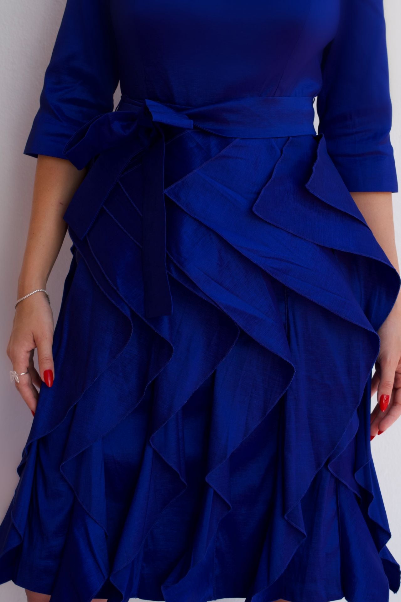 Close up royal blue taffeta dress with waist tie and ruffle skirt, styled for an elegant cocktail or special occasion look