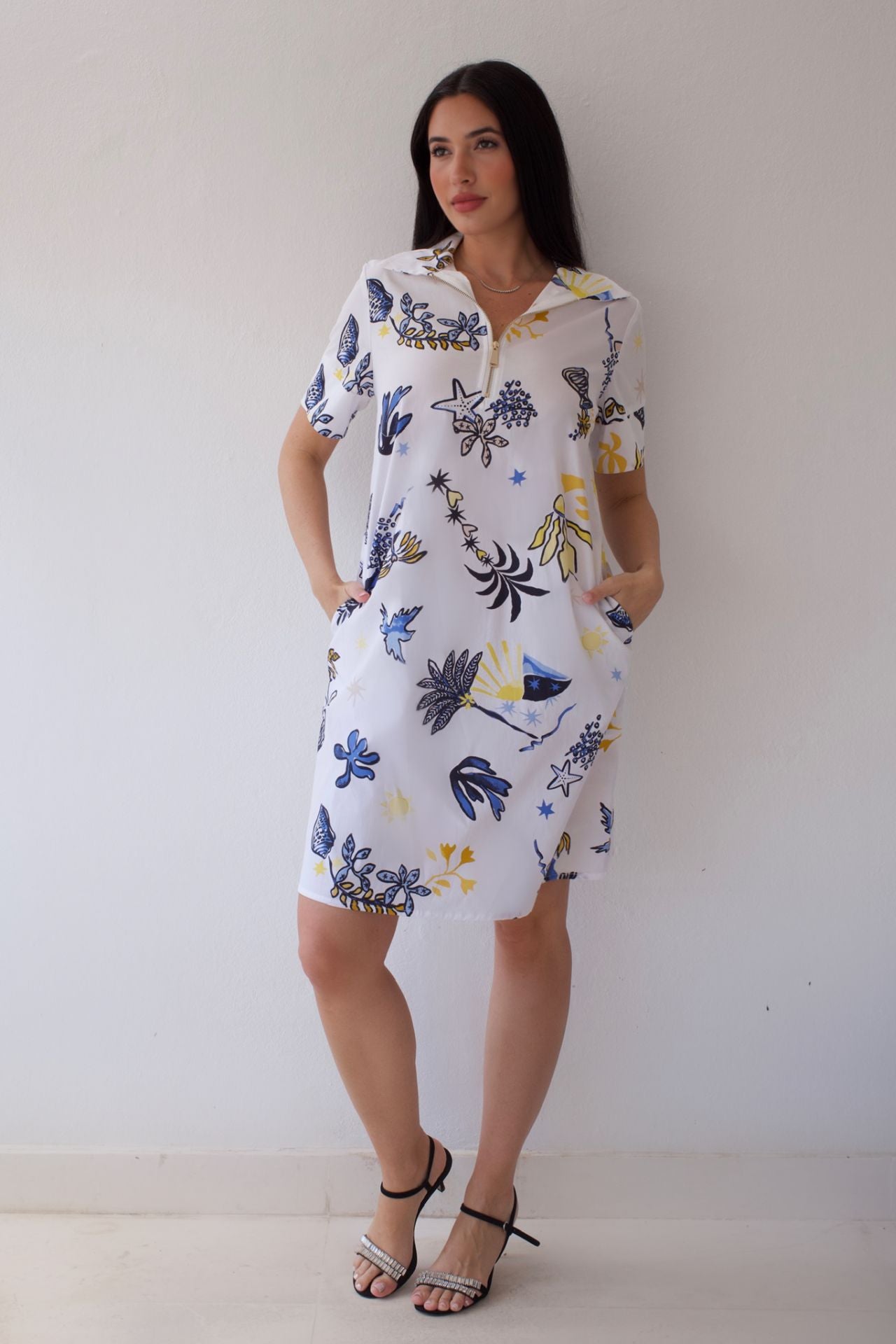 Woman wearing a white dress with colorful floral pattern against a plain background