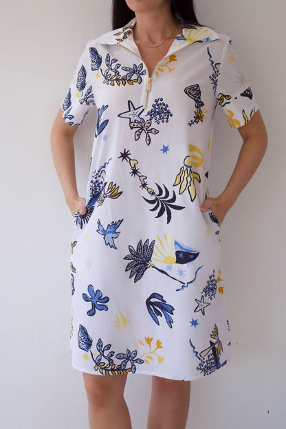 Woman wearing a white dress with coastal sketch pattern against a plain background