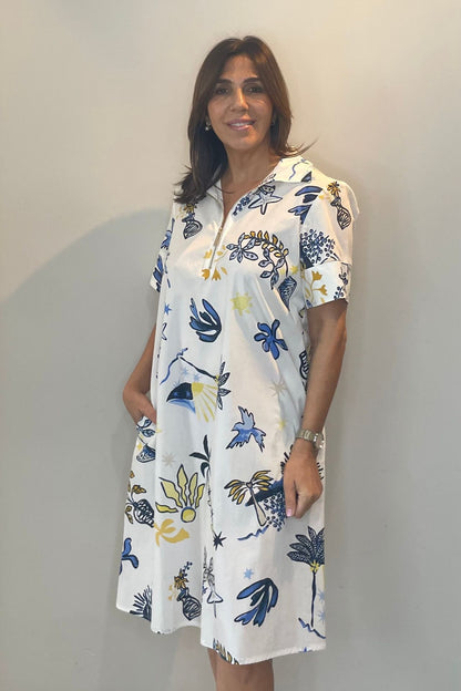 Woman wearing a white dress with blue and yellow floral patterns against a plain background