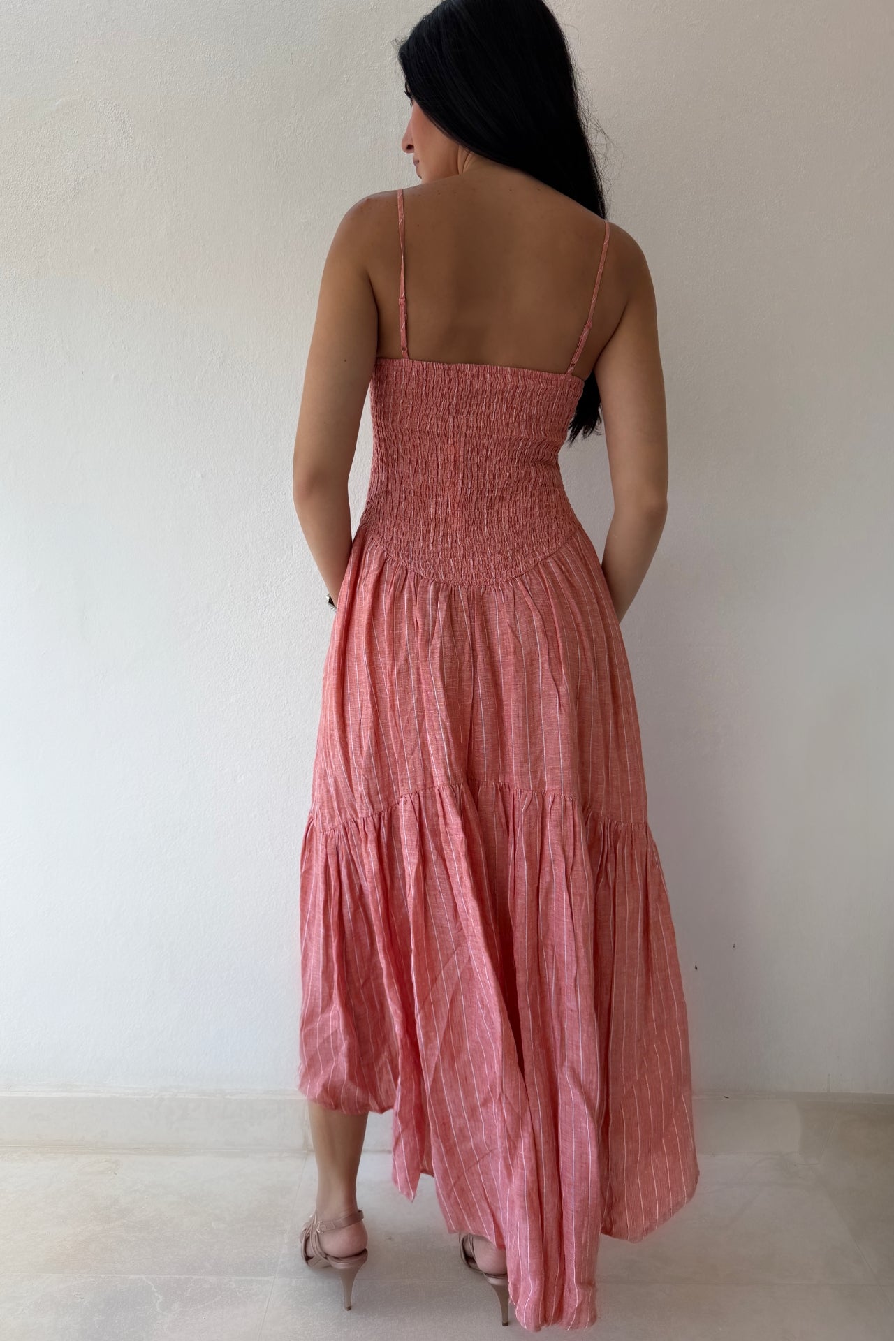 Model wearing the Coastal Sunset Midi Dress in a soft coral linen fabric featuring adjustable straps, a fitted bodice, and a flowing tiered midi skirt.