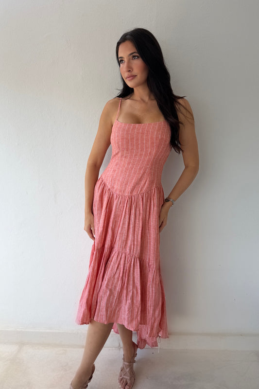 Model wearing the Coastal Sunset Midi Dress in a soft coral linen fabric featuring adjustable straps, a fitted bodice, and a flowing tiered midi skirt.