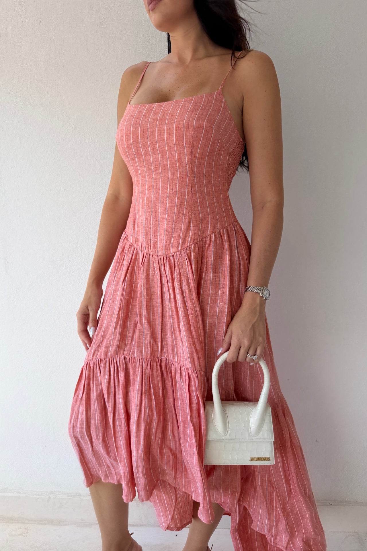 Model wearing the Coastal Sunset Midi Dress in a soft coral linen fabric featuring adjustable straps, a fitted bodice, and a flowing tiered midi skirt.