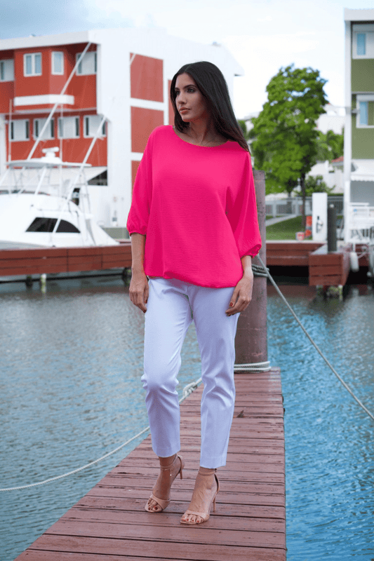 A woman standing on a dock wearing a hot pink top and white pants.