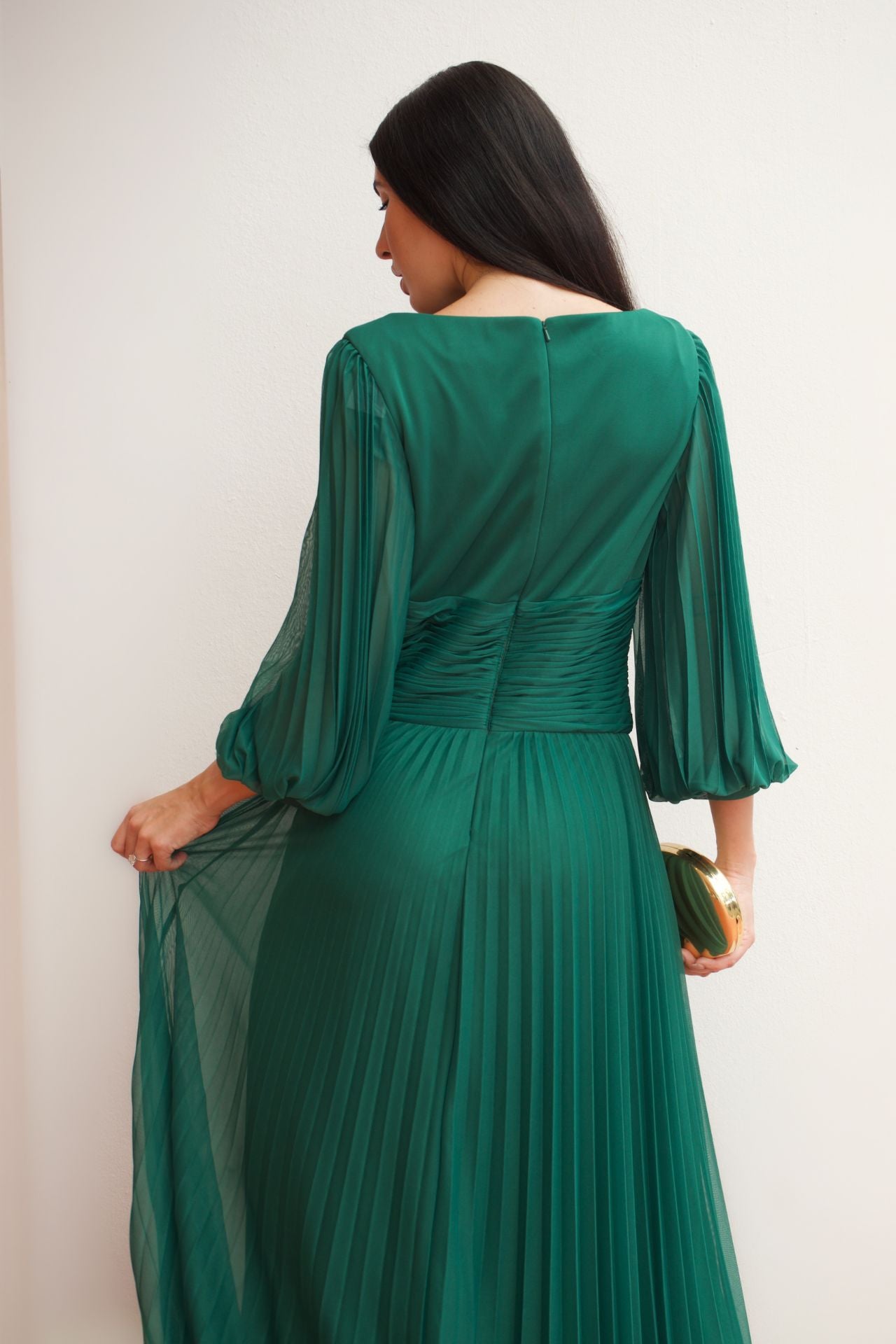 Model wearing an emerald green pleated wrap formal gown with long sleeves and flowing skirt.
