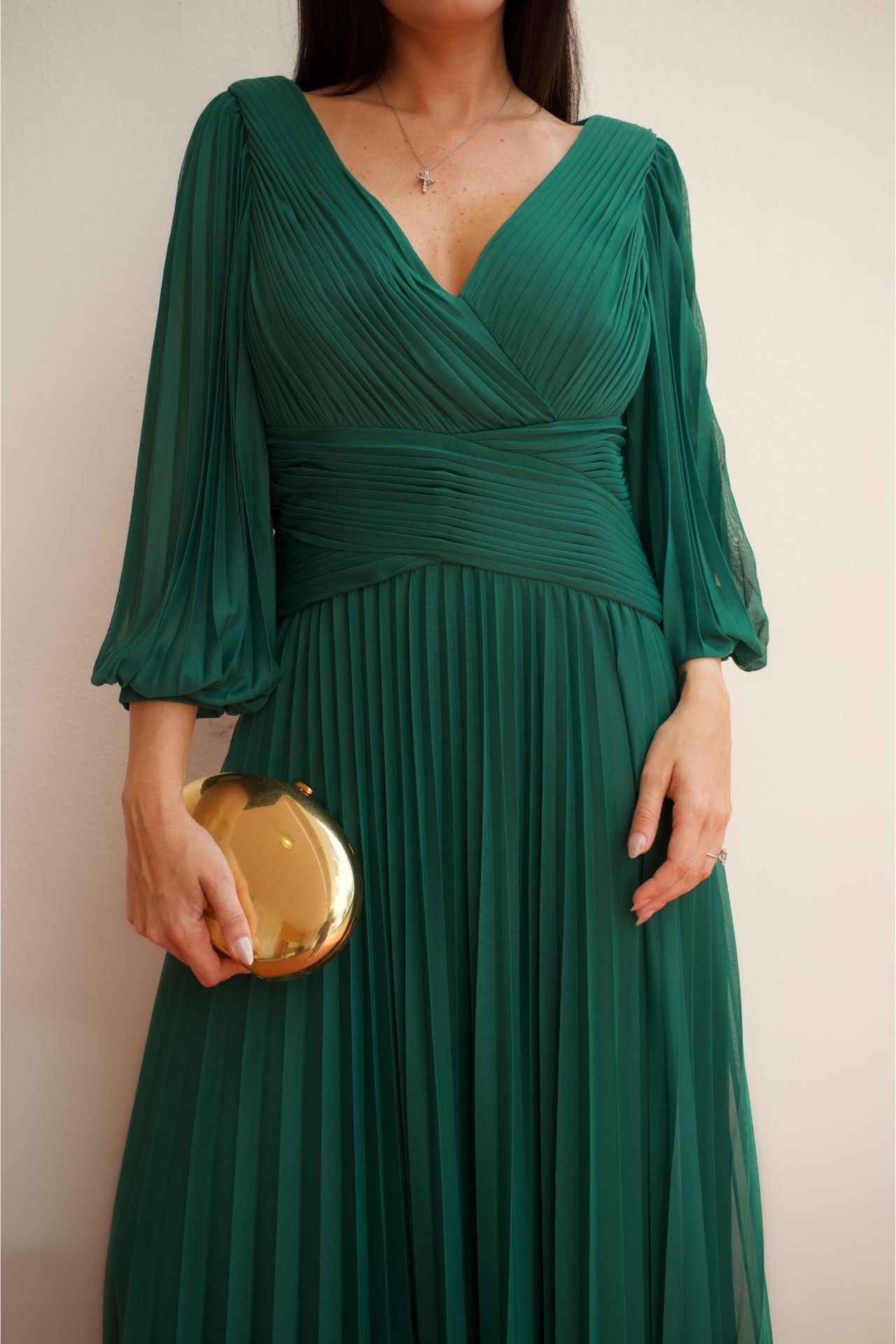 Model wearing an emerald green pleated wrap formal gown with long sleeves and flowing skirt.