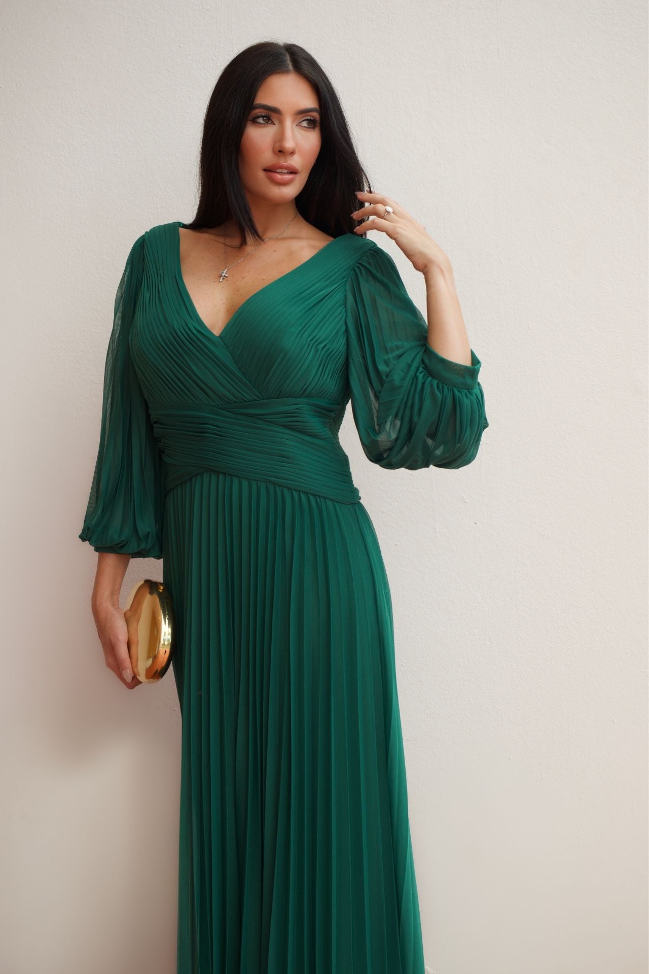 Model wearing an emerald green pleated wrap formal gown with long sleeves and flowing skirt.