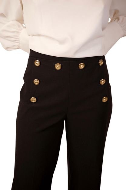 A woman wearing high waisted wide leg cropped sailor pants in black color with a white top.
