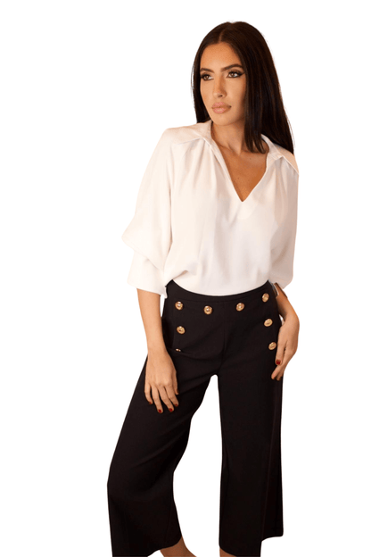 A woman wearing high waisted wide leg cropped sailor pants in black color with a white top.
