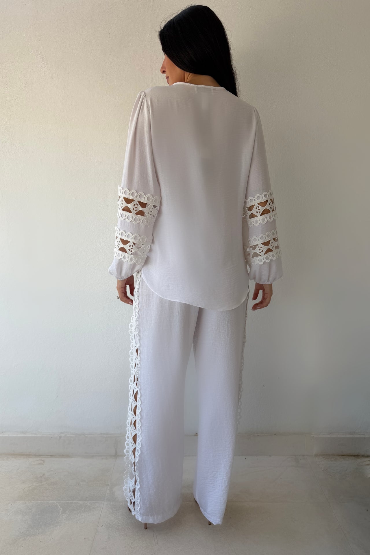 Model wearing the Island Breeze Pant Set featuring a white long sleeve blouse with decorative cutout trim and coordinating wide-leg pants.
