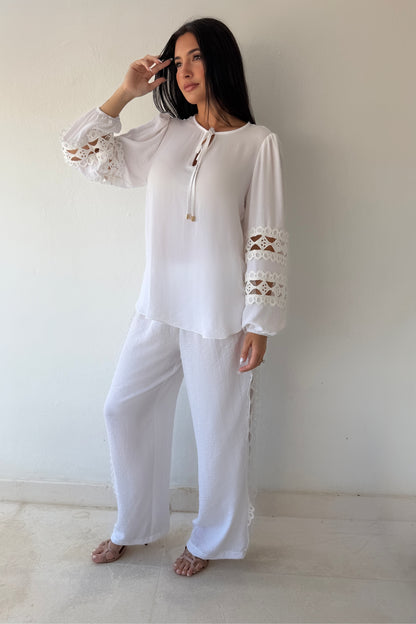 Model wearing the Island Breeze Pant Set featuring a white long sleeve blouse with decorative cutout trim and coordinating wide-leg pants.