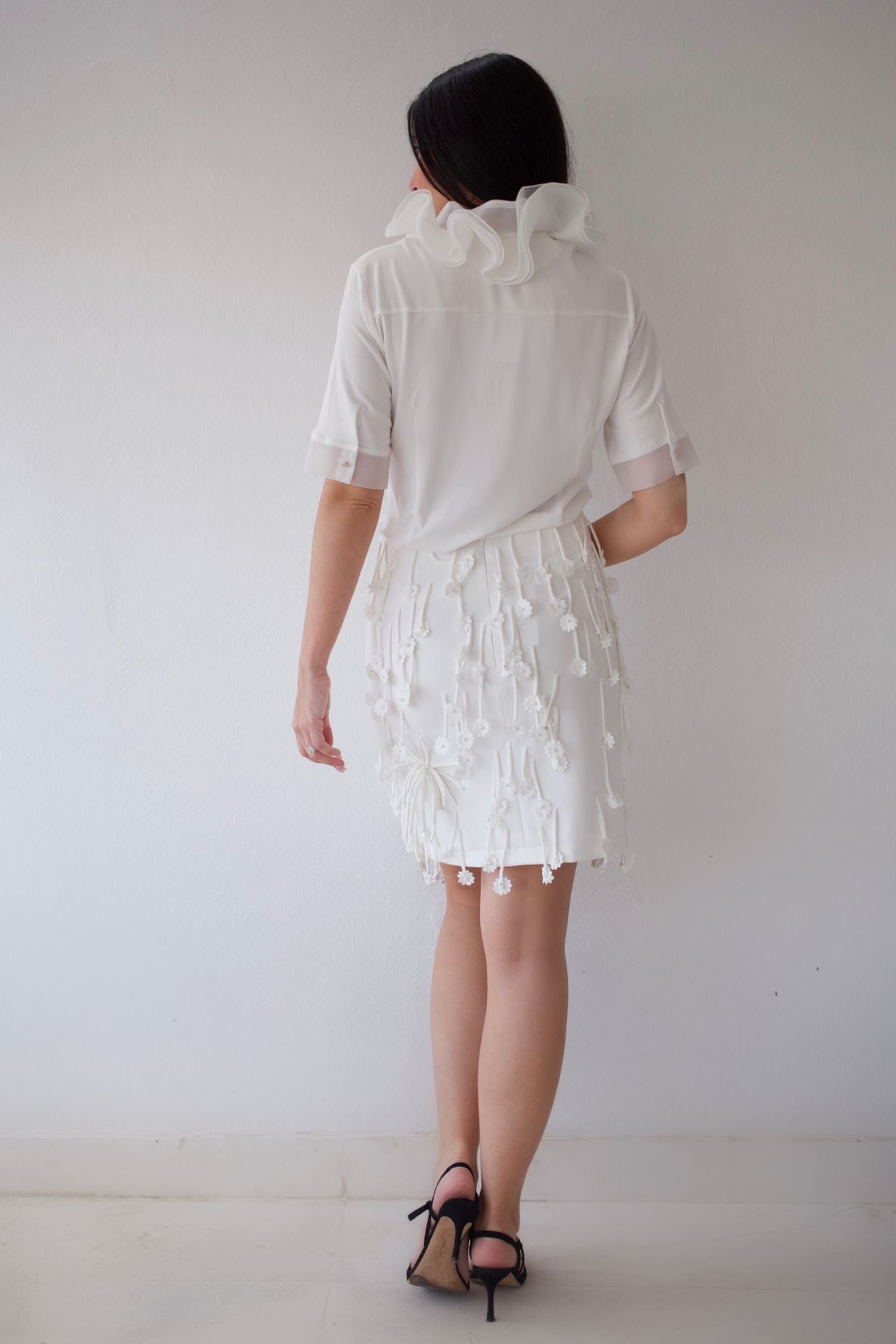 Person wearing a white skirt set with ruffled details against a plain background