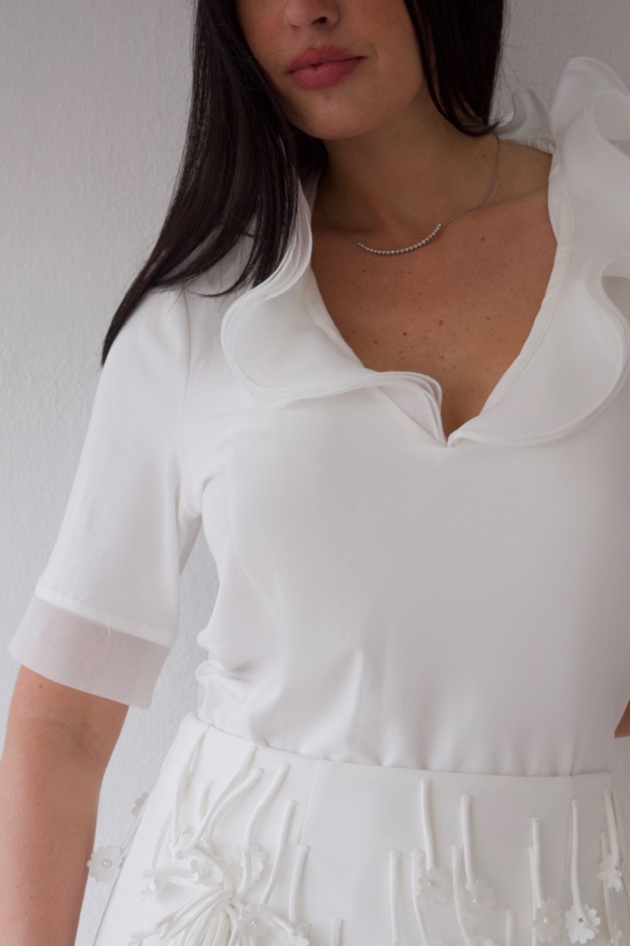 White blouse with ruffled neckline worn by a person against a neutral background