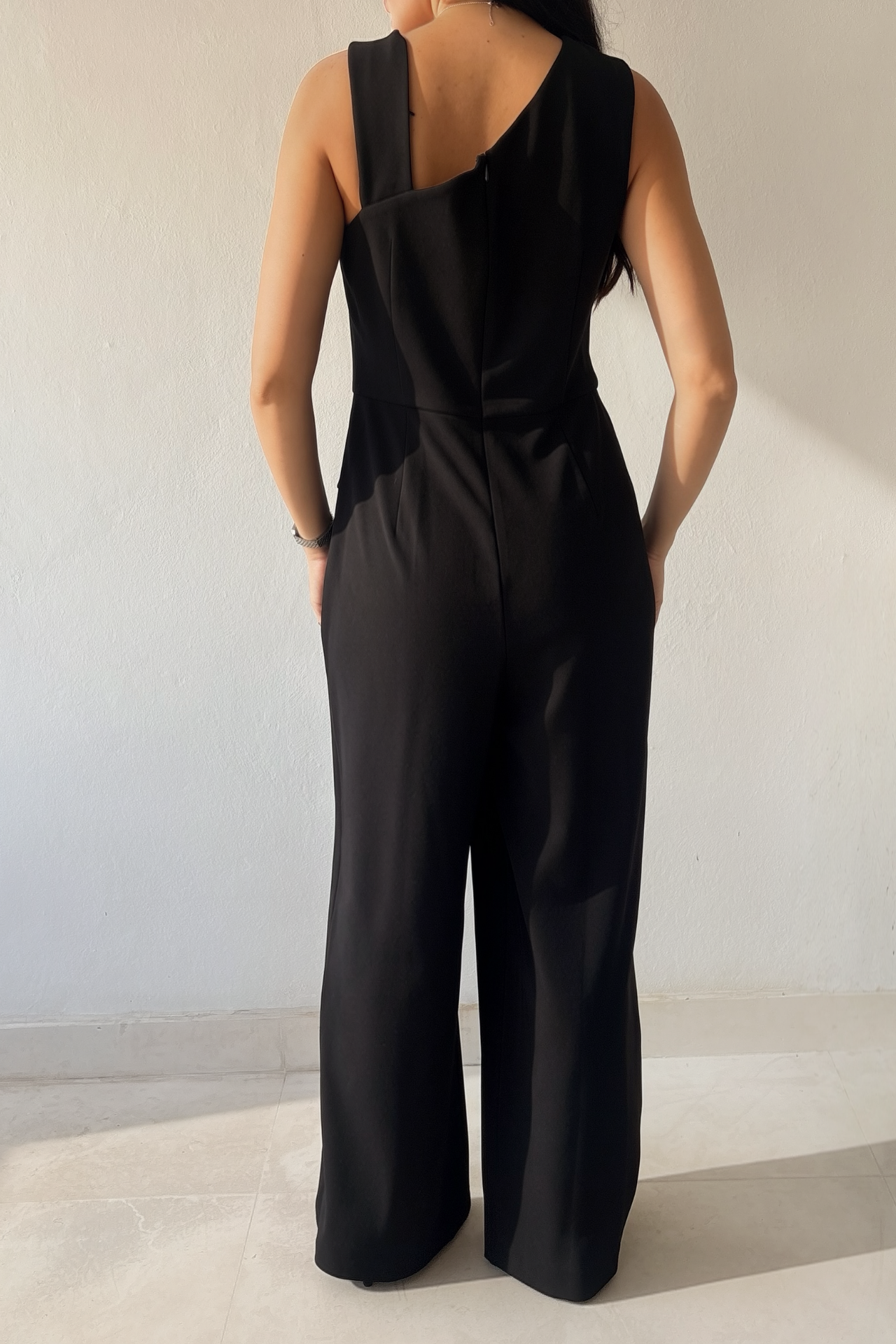 Woman wearing the Midnight Grace Jumpsuit, a black wide-leg jumpsuit with asymmetrical draping, gold-tone shoulder buckle and front overlay.