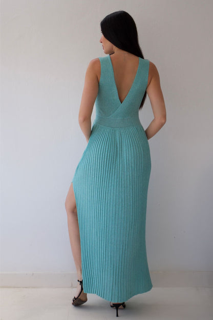 Woman wearing a mint dress with a deep neckline and slit on a plain background