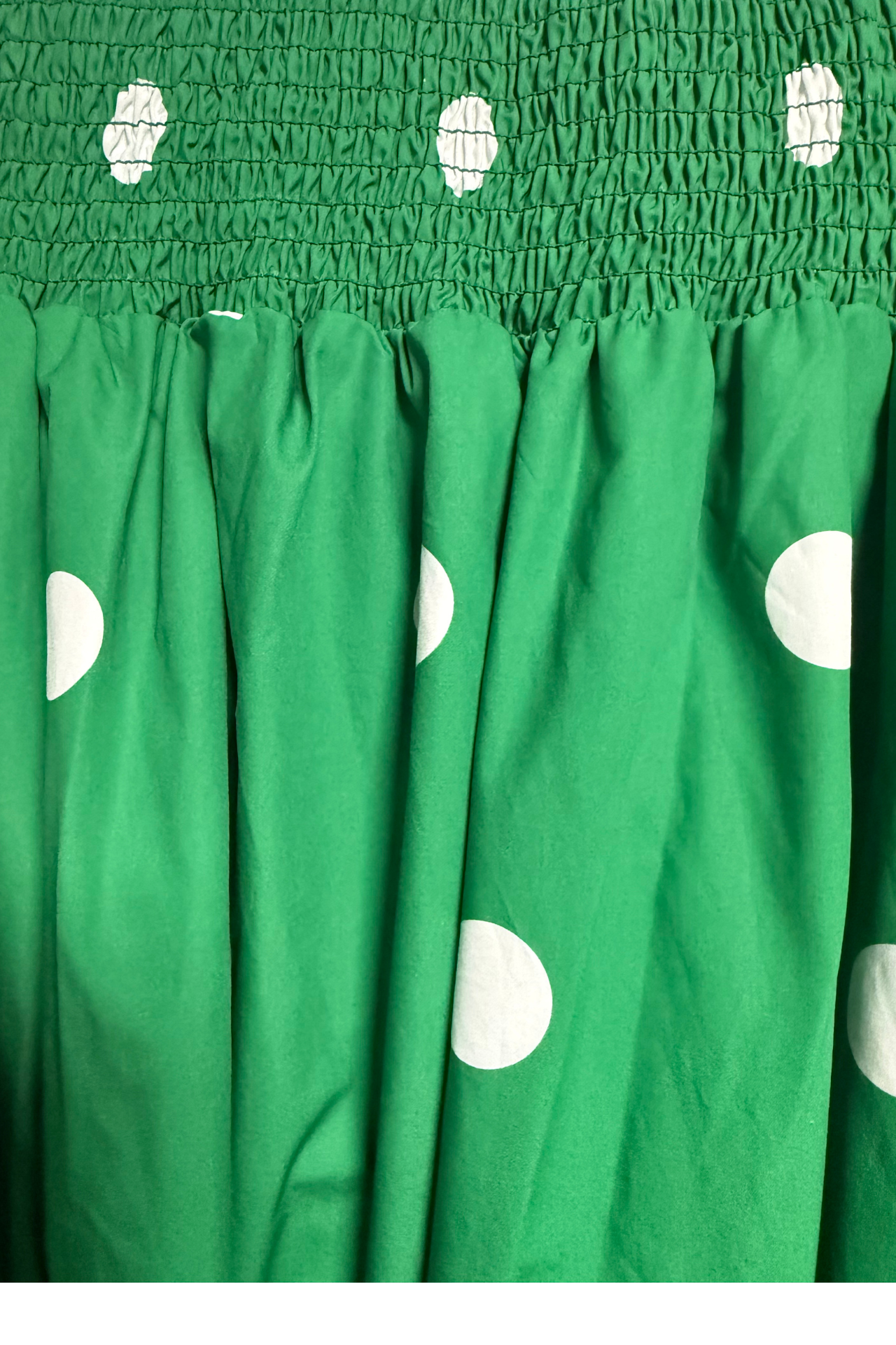Green fabric with large white polka dots and a smocked elastic top section.