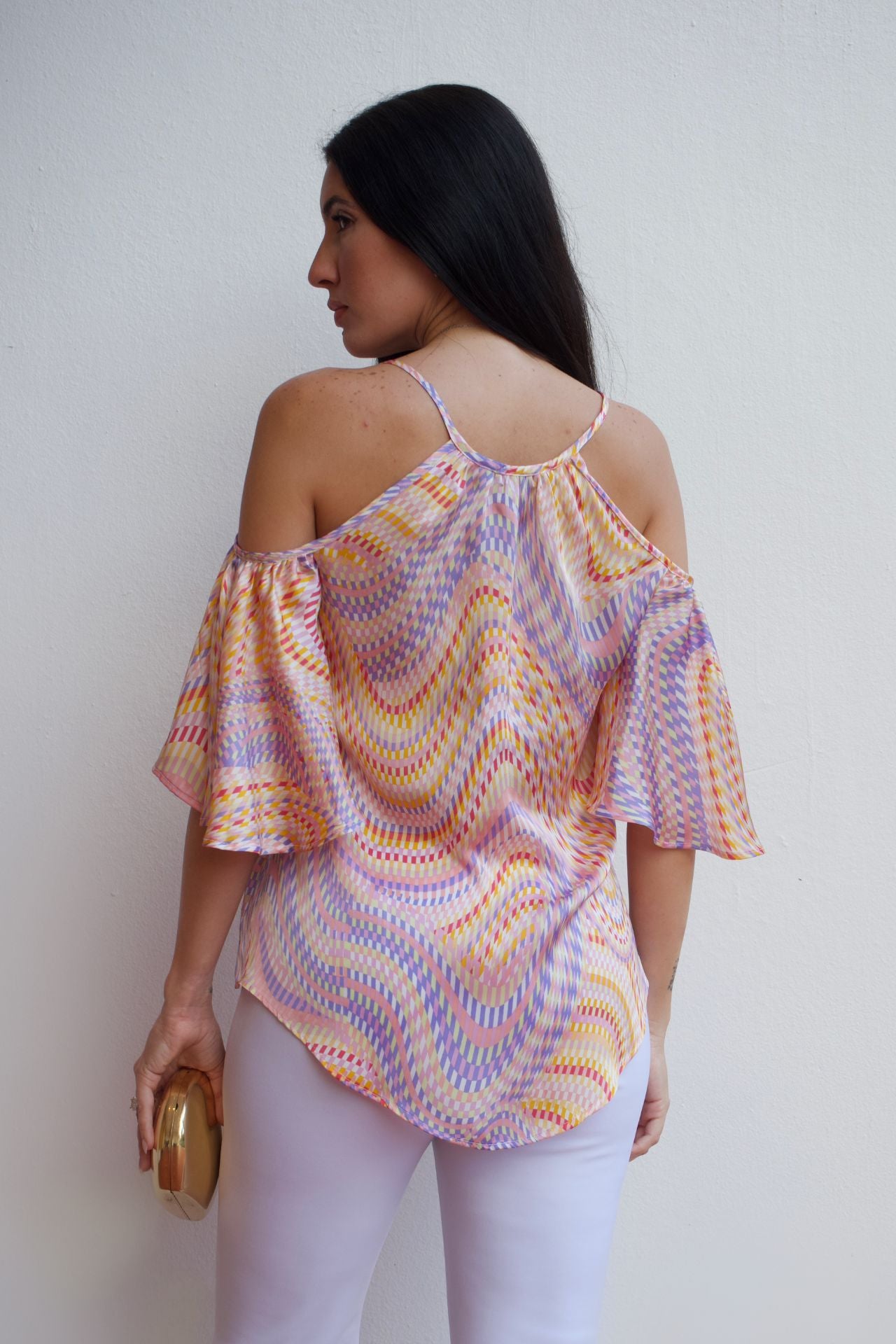 Woman wearing a multicolor mosaic off-shoulder top with cold-shoulder sleeves and a relaxed fit, paired with light-colored pants.