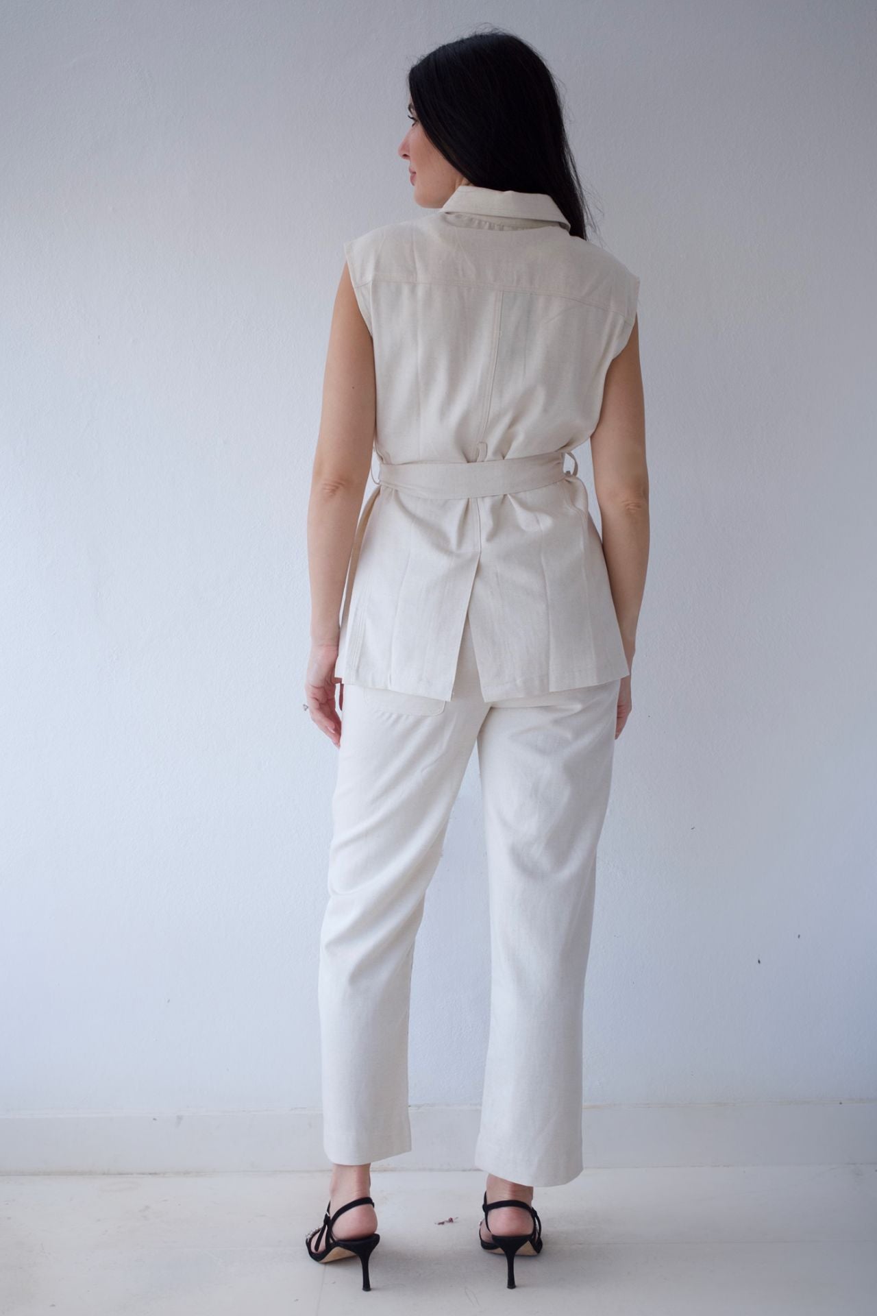 Woman wearing a natural sleeveless top and pants against a plain background