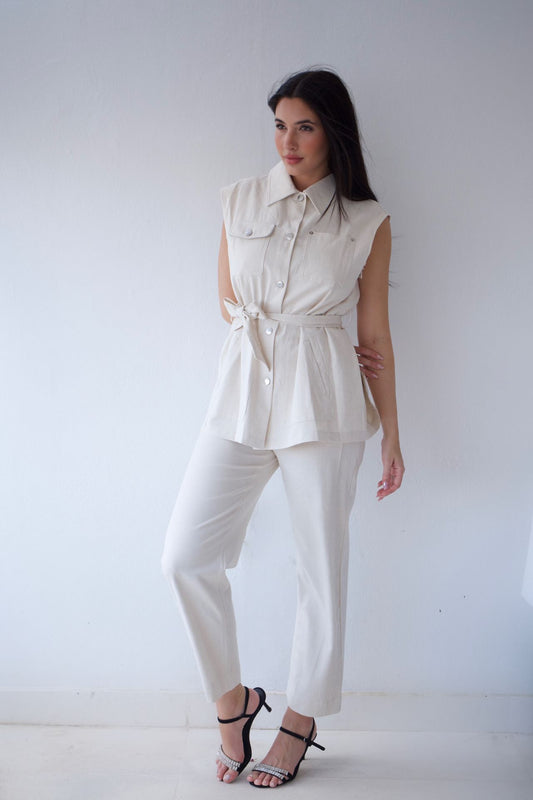 Woman wearing a natutal sleeveless top and pants against a plain background
