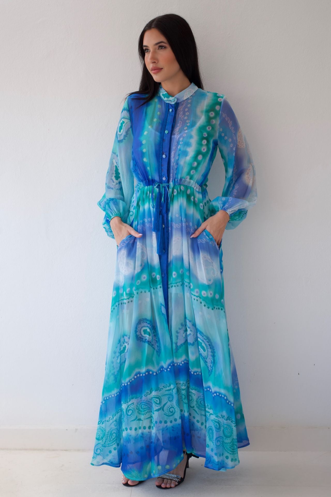 Woman wearing a long, patterned dress with blue and green colors against a white background