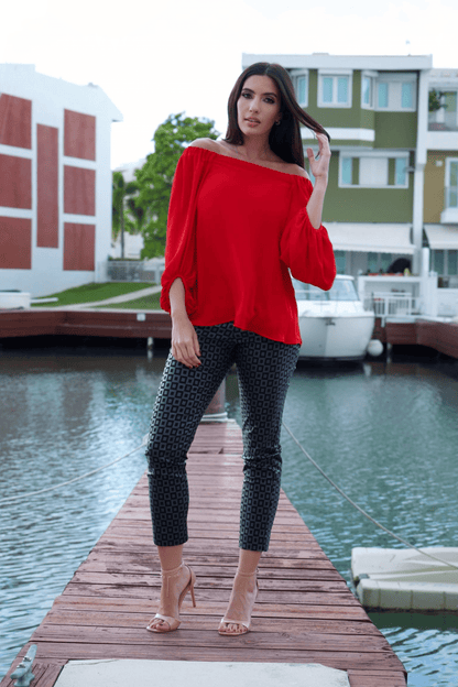 A woman wearing a vibrant red, off-shoulder long sleeve top with a crew neckline, paired with black patterned pants. The top features a loose fit and long bubble sleeves.