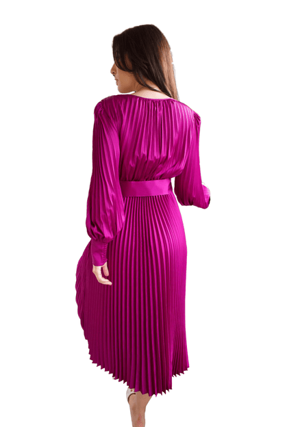 A model wearing a magenta pleated v-neck satin dress with long bubble sleeves and a floral detail on the belt, paired with open-toe heels.