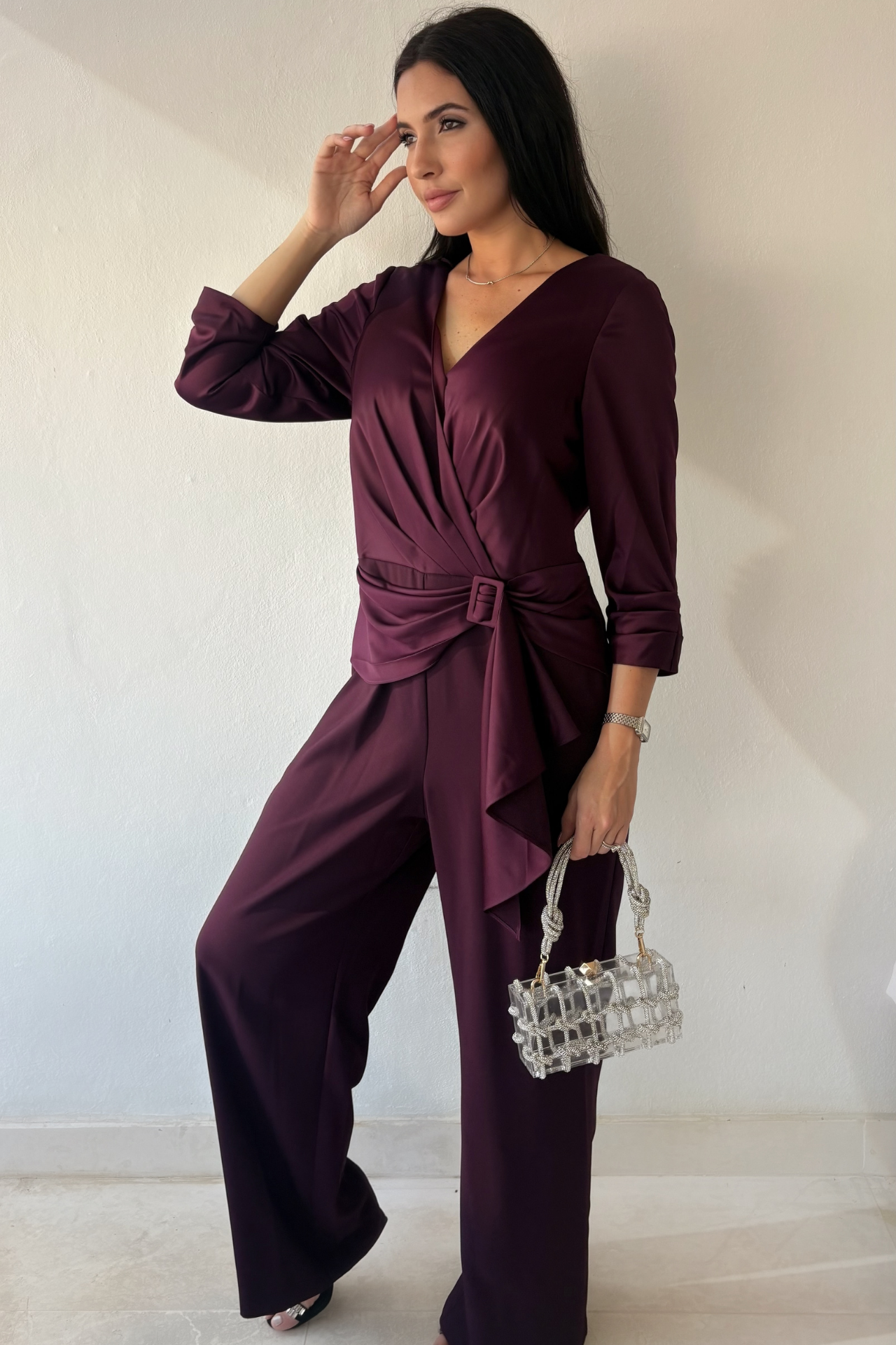 Woman wearing the Plum Elegance Jumpsuit with V-neckline, draped buckle waist, three-quarter sleeves and wide-leg silhouette.